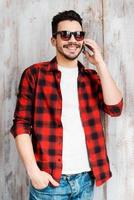 Enjoying good talk. Handsome young man talking on the mobile phone and smiling while standing against the wooden wall photo