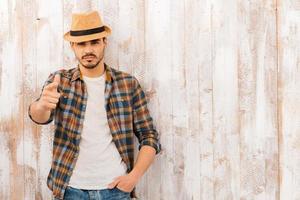 él te elige a ti. retrato de un joven apuesto mirando y señalando a la cámara mientras está de pie contra la pared de madera foto