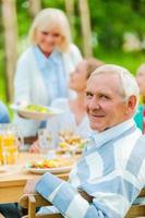 Proud to have a big family. Happy family sitting at the dining table outdoors while senior man looking over shoulder and smiling photo