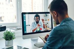 Young man talking to collegue by video call while sitting in office photo