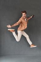 Crazy man in mid-air. Full length of playful young man listening music while jumping against grey background photo