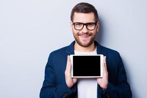 copie el espacio en su tableta. un joven alegre sosteniendo una tableta digital y sonriendo mientras se enfrenta a un fondo gris foto