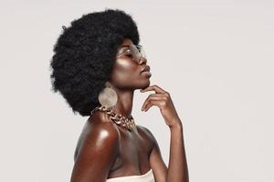 Side view of beautiful young African woman in golden jewelry keeping eyes closed and touching face photo