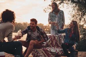 momento de verdadera alegría. grupo de jóvenes con ropa informal sonriendo y brindando mientras disfrutan de una fiesta en la playa cerca del lago foto