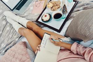 Close up top view of young woman in pajamas writing something down while resting in bed at home photo