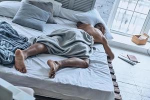 Impossible to wake up. Top view of young African man sleeping while lying in the bed at home photo