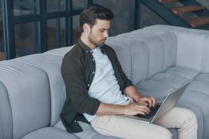 Handsome young man using laptop while sitting on the sofa at home photo