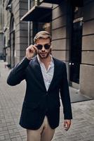 In his own style. Handsome young man in smart casual wear adjusting his eyewear while walking through the city street photo