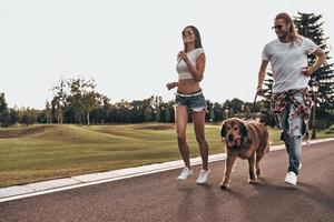 Love inspires them. Full length of beautiful young couple running with their dog while spending time outdoors photo