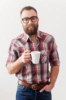 Cafe mañanero. apuesto joven con gafas de pie con una taza de café y mirando a la cámara foto