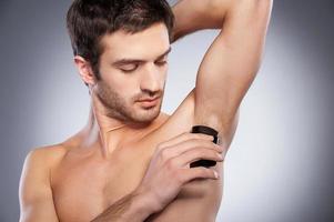 Staying fresh. Confident young shirtless man using dry deodorant while standing isolated on grey background photo