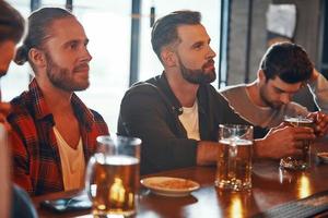 Group of young men in casual clothing enjoying beer while watching TV in the pub photo