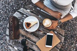 Little coffee break. Close-up top view of young woman holding a cup of coffee while sitting in restaurant outdoors photo