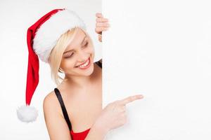 Pointing a copy space. Beautiful young woman in Santa costume looking out of the copy space and pointing it while standing isolated on white photo