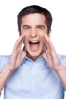 Announcing good news. Handsome young man in blue shirt at camera and shouting while standing isolated on white photo