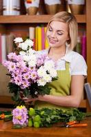 Flowers arrangement. Beautiful young blond hair woman in apron arranging flowers and smiling photo