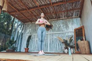 Full length of beautiful young woman in sports clothing meditating on patio photo