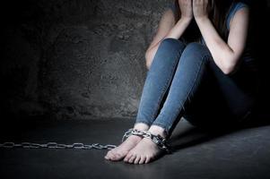 Trapped woman. Young woman trapped in chains covering face with hands while sitting on the floor in a dark room photo