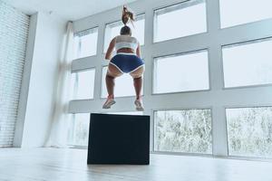 salto largo. vista trasera de una joven con ropa deportiva saltando mientras hace ejercicio en el gimnasio foto