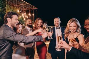 grupo de personas hermosas en ropa formal comunicándose y sonriendo mientras pasan tiempo en una fiesta de lujo foto