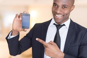 Businessman with mobile phone. Cheerful young African man in formalwear holding a mobile phone and pointing it photo