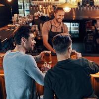 jóvenes sonrientes con ropa informal bebiendo cerveza mientras se sientan juntos en el pub foto