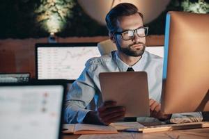 Confident young man working on computer while staying late in the office photo