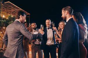 grupo de personas hermosas en ropa formal brindando con champán y sonriendo mientras pasan tiempo en una fiesta de lujo foto