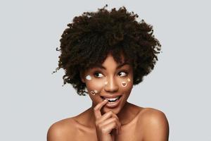 Happiness highlights her beauty. Attractive young African woman looking away and smiling while standing against grey background photo