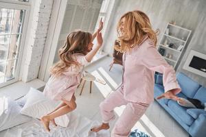 Top view of cute little girl jumping on the bed with her mother while spending time at home photo