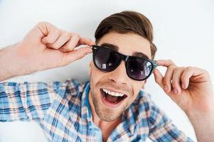 Carefree fun. Top view of cheerful young man adjusting eyewear while standing against white background photo