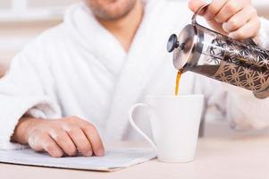 sirviendo café recién hecho. imagen recortada de un hombre en bata de baño sirviendo café en la taza foto