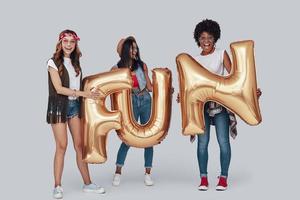 longitud total de tres mujeres jóvenes atractivas que llevan globos y sonríen mientras están de pie contra el fondo gris foto