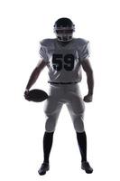 Full of forces and energy.  Full length of American football player holding ball and looking ay camera standing against white background photo