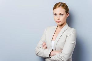 Confident businesswoman. Confident young businesswoman keeping arms crossed while standing against grey background photo