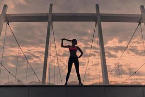 Real freedom. Full length of modern young woman in sports clothing keeping hand on hip and touching her hair while standing outdoors photo