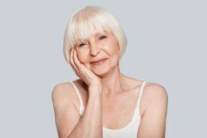 Time for yourself. Beautiful senior woman looking at camera and smiling while standing against grey background photo