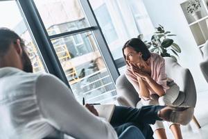 Trying to find a peace. Young frustrated woman solving her mental problems while sitting on the therapy session with psychologist photo