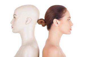 Real and artificial. Side view of beautiful young shirtless woman standing her back to the mannequin and looking away while isolated on white background photo
