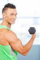 Working out. Muscular man lifting weights and looking at the camera photo