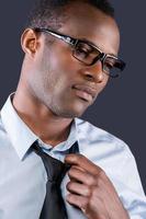 Taking his necktie off. Handsome young black man taking off his necktie while standing against grey background photo