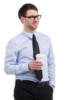 Coffee break. Confident young man in shirt and tie holding a cup of coffee and looking away while standing isolated on white photo