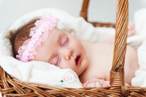linda durmiente. pequeño bebé durmiendo mientras está acostado en una canasta de mimbre y cubierto con una toalla foto