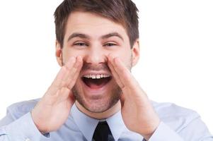 anunciando buenas noticias. joven feliz con camisa y corbata gritando mientras mira la cámara y aislado de fondo blanco foto