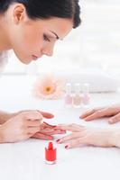 haciendo manicura roja. primer plano de esteticista haciendo manicura roja a una clienta foto