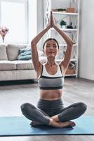 golpeando la pose. bella joven asiática vestida con ropa deportiva haciendo yoga mientras se relaja en casa foto