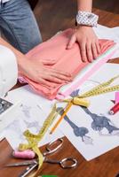 The best quality textile for the most creative looks. Close-up top view of tailor adjusting a stack of multi colored textile laying on the table with other sewing items on it photo