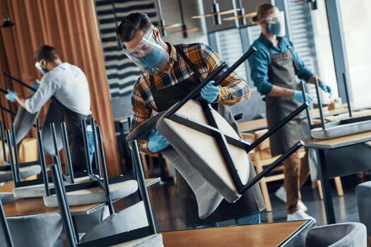 tres hombres con protectores faciales y delantales arreglando muebles en el restaurante foto