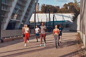 toda la longitud de los jóvenes en ropa deportiva corriendo juntos al aire libre foto