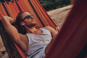 Resting after a long day. Handsome young man keeping hand behind head while lying in hammock photo